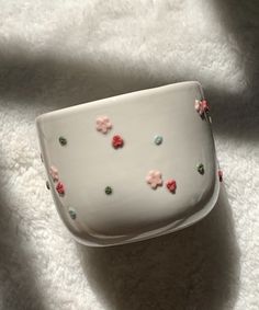 a white bowl with pink and green flowers on it sitting on top of a blanket