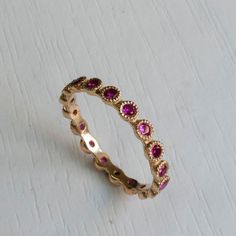 Gold Eternity ring set with Beautiful Pink Rubies. Famous for its passionate Pink-Red Color this July birthstone gemstone in one of finest and most sought after gemstones. Elegantly Set in a crown settings, Each ruby is 2mm in diameter with excellent color and clarity. This graceful Eternity ring has a dainty poise about it, getting lots of the right attention every time you wear it on its own or stack it with your other rings! Featuring between 15-22 Gemstones(Depending on ring size). Other sto Elegant Red Eternity Band As A Gift, Pink Eternity Band With Prong Setting As Promise Ring, Pink Sapphire Stackable Ring For Anniversary, Elegant Stackable Ruby Birthstone Ring, Pink Lab-created Ruby Ring, Pink Ruby Rings With Prong Setting, Pink Sapphire Halo Ring Jewelry, Pink Gold Ruby Ring With Prong Setting, Pink Cubic Zirconia Ruby Ring With Prong Setting