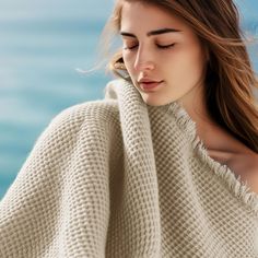 a beautiful young woman wrapped in a blanket by the ocean looking down at her face