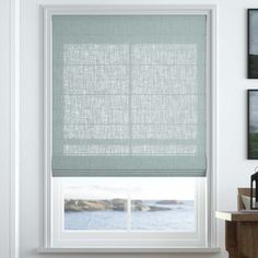 a window with roman shades in a room next to a table and pictures on the wall