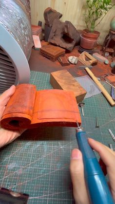 a person is cutting an orange piece of leather with a pair of scissors and pliers