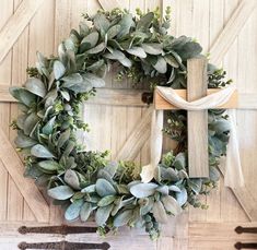 a wreath is hung on the front door with a cross and greenery around it