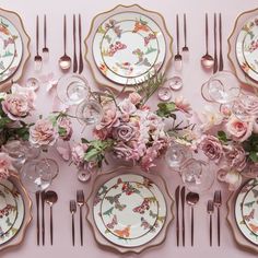 the table is set with pink flowers and gold trimmings, plates and silverware