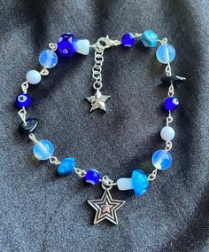 Blue beaded silver charm bracelet with stars, beads, beaded rocks, and evil eyes. Blue Bohemian Jewelry With Star Charm, Bohemian Blue Jewelry With Star Charm, Bohemian Blue Star Charm Jewelry, Blue Star-shaped Jewelry With Colorful Beads, Blue Star-shaped Bohemian Jewelry, Handmade Celestial Beaded Bracelets With Round Beads, Blue Beaded Bracelets With Silver Beads For Festivals, Celestial Style Beaded Bracelets As Gift, Bohemian Star-shaped Beaded Bracelet