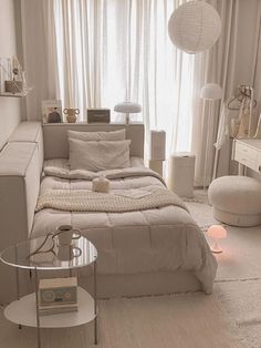 a bedroom with a bed, couch and table in front of a large white curtained window