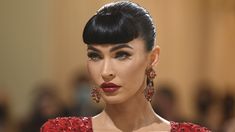 a woman with black hair and red lipstick wearing large earrings on her head, looking off to the side