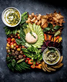 a platter filled with vegetables and dips on top of a black countertop