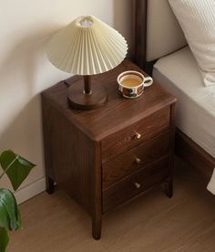 a nightstand with a cup of coffee on it next to a bed