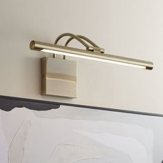 a wall mounted light on the side of a white wall next to a framed painting