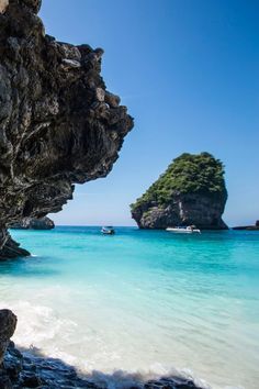 the water is crystal blue and there are boats in the distance on the beach near some rocks