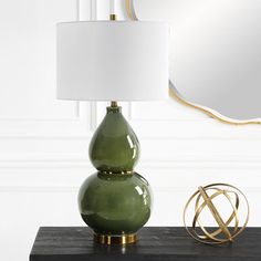 a green lamp sitting on top of a black table next to a mirror and a gold sculpture