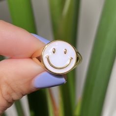 a person holding a ring with a smiley face on it's middle finger, in front of a potted plant