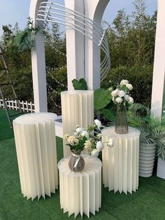 three white vases with flowers in them sitting on the grass