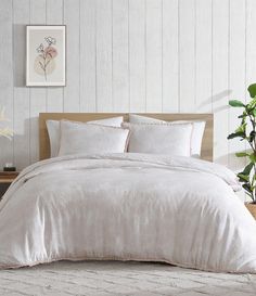 a bed with white sheets and pillows in a room next to a potted plant