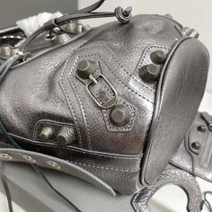 Balenciaga &apos;s popular "Le Cagole" series is a modern interpretation of its "City" handbags - reshaped into a bucket bag design to inject a new soul into it. The large size adds two round top handles, combining classic and Modern trends are perfectly integrated. On the basis of retaining the original DNA of the motorcycle bag&apos;s flat rivets, delicate buckles and tassel zippers, it adds adjustable woven shoulder straps and a cute and playful heart-shaped mirror, which Silver-tone Hardware Bucket Shoulder Bag For Shopping, Luxury Crossbody Bucket Bag With Silver-tone Hardware, Luxury Bucket Bag With Silver-tone Hardware, Silver Balenciaga Bag, Silver Bucket Bag With Silver-tone Hardware, New Soul, Shaped Mirror, Motorcycle Bag, Lv Shoes