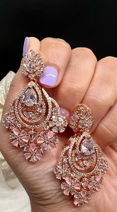 a woman's hand holding two pairs of pink and white diamond chandeliers