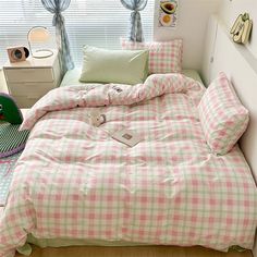 a bed with pink and green checkered comforter in a bedroom next to a window