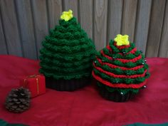 three knitted christmas trees sitting on top of a red table cloth next to a pine cone