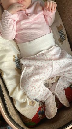 a baby is laying in a basket with her hand on her chin and looking at the camera