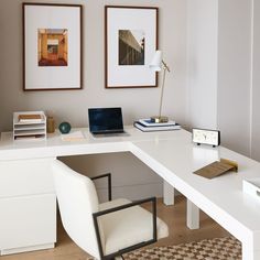 a white desk topped with a laptop computer next to a lamp and pictures on the wall