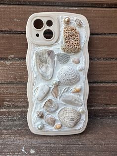 an iphone case with shells and seashells on the back, sitting on a wooden surface