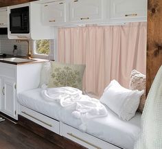 a kitchen area with a sink, microwave and window in the back ground is covered by pink curtains