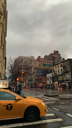 a yellow taxi cab driving down a street next to tall buildings on a cloudy day