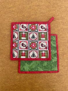 two red and green placemats with christmas decorations on them sitting on a brown surface