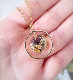 a hand holding a gold filled necklace with flowers inside the circle on it's chain