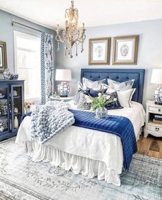 a blue and white bedroom with chandelier, bed, nightstands and pictures on the wall