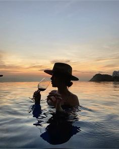 a woman holding a wine glass in her hand while standing in the water at sunset