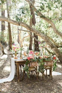 a table with flowers and candles on it in the woods