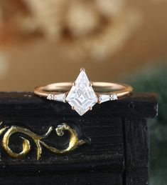 a close up of a diamond ring on a black box with gold lettering in the background