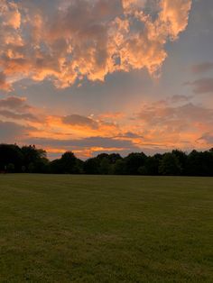 a field with trees and clouds in the background at sunset or sunrise hours before dawn