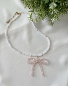 Measurements: 16 to 18.5 inches long Total Weight: 0.45 oz Add a sweet and playful touch to your look with this charming bow necklace, crafted from pink and white glass beads. The delicate bow design brings a whimsical flair, while the shimmering beads catch the light beautifully. Finished with a durable stainless steel clasp, this necklace combines elegance and practicality, making it perfect for everyday wear or adding a dash of fun to special occasions. It's a unique, handcrafted piece that's both eye-catching and timeless. Pink Bow Necklace For Party, Elegant White Jewelry With Pink Bow, White Ribbon Necklace For Gift, Adjustable Pink Ribbon Necklace, Pink Pearl Beaded Necklace Gift, Pink Pearl Beaded Necklace For Gift, Cute White Jewelry With Beaded Chain, White Necklace With Butterfly Knot For Gift, Cute White Jewelry With Ribbon