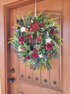 a wreath hanging on the front door of a house decorated with flowers and greenery