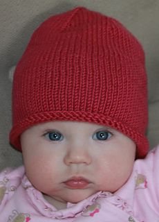 a baby with blue eyes wearing a red knitted hat