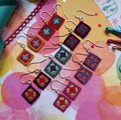 a bunch of small square earrings sitting on top of a table next to some scissors