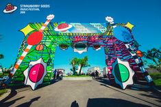 the entrance to an art festival is decorated in bright colors and shapes with people standing under it