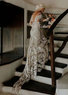 a woman is standing on the stairs with flowers in her hand and wearing a long white dress