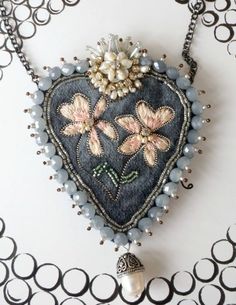 an embroidered heart with flowers and pearls hanging on a chain