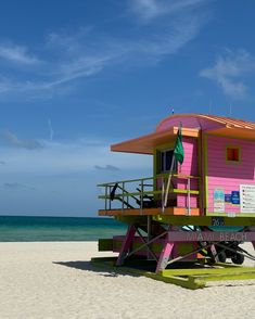 a pink and green lifeguard stand on the beach with blue skies in the background