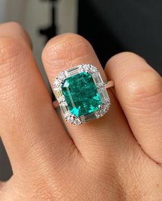 a woman's hand holding an emerald and diamond ring