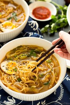 someone holding chopsticks over a bowl of noodles with an egg in the middle