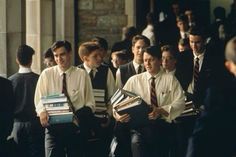 a group of young men standing next to each other in front of a building holding books