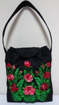 a black purse with red roses on it and green leaves in the middle, sitting on a white surface