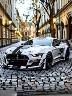 a white sports car parked on the side of a cobblestone road in front of tall buildings