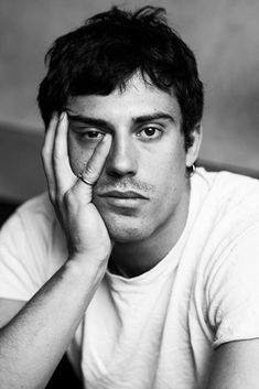 a black and white photo of a man holding his hand to his face while looking at the camera