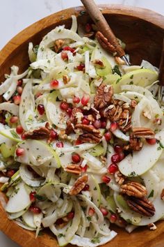 a wooden bowl filled with apples, onions and pecans on top of a table