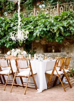 a table set up with white linens and gold chairs for an outdoor wedding reception